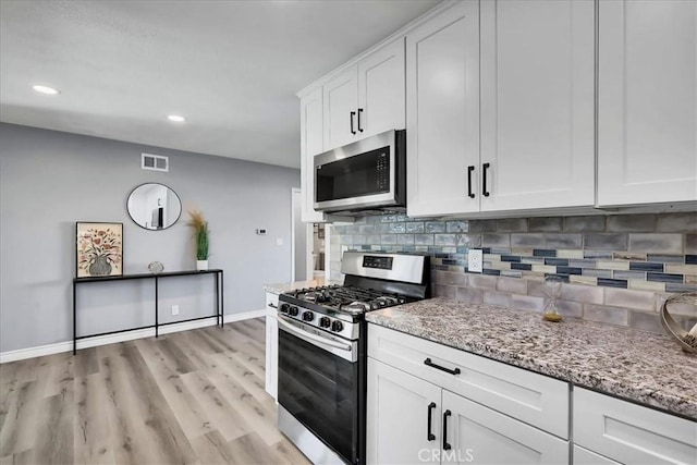 kitchen with white cabinetry, appliances with stainless steel finishes, light stone counters, decorative backsplash, and light hardwood / wood-style flooring