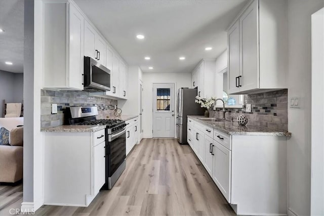 kitchen with light hardwood / wood-style floors, stainless steel appliances, sink, white cabinets, and tasteful backsplash