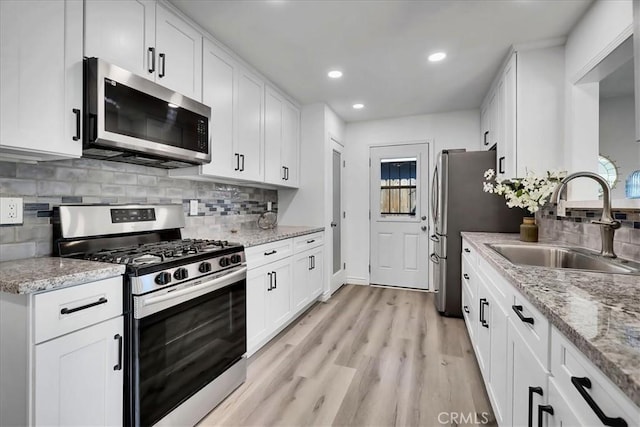 kitchen with light stone countertops, light wood-type flooring, white cabinets, appliances with stainless steel finishes, and sink