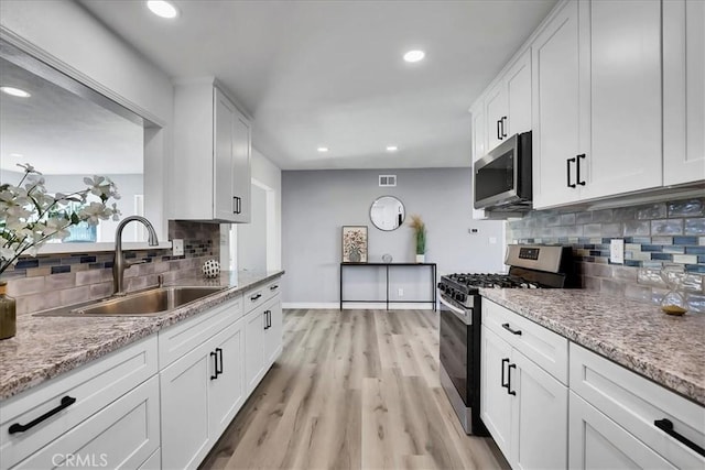 kitchen with sink, light stone countertops, appliances with stainless steel finishes, and white cabinetry