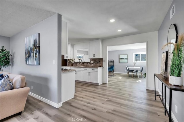 interior space with light hardwood / wood-style floors, a textured ceiling, sink, white cabinetry, and backsplash