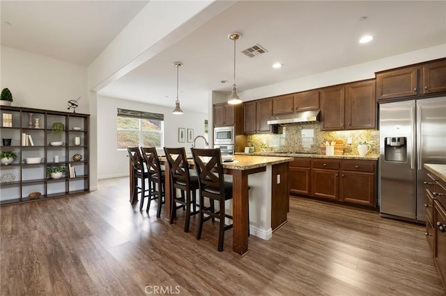 kitchen featuring built in appliances, a kitchen breakfast bar, hanging light fixtures, light stone countertops, and a kitchen island with sink