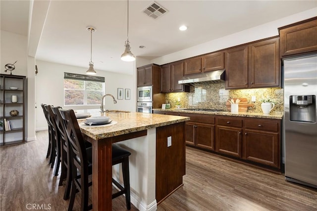 kitchen featuring stainless steel appliances, sink, a breakfast bar area, hanging light fixtures, and a center island with sink