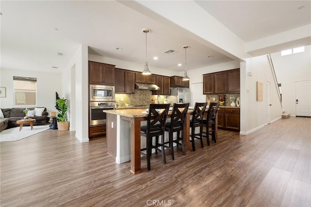 kitchen featuring a kitchen breakfast bar, a kitchen island with sink, stainless steel appliances, light stone counters, and decorative light fixtures