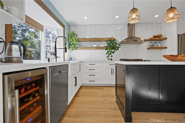 kitchen featuring beverage cooler, hanging light fixtures, white cabinets, wall chimney range hood, and tasteful backsplash