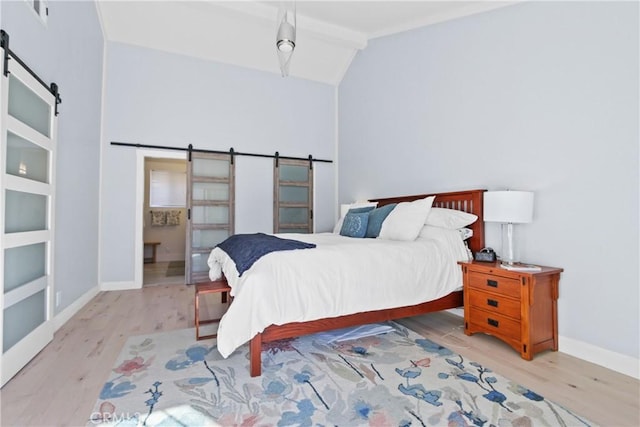 bedroom featuring connected bathroom, vaulted ceiling, a barn door, and light hardwood / wood-style flooring