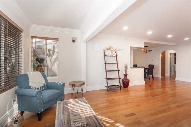 sitting room featuring light wood finished floors, baseboards, arched walkways, and crown molding