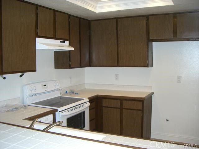 kitchen featuring tile counters, electric range, a tray ceiling, crown molding, and dark brown cabinets