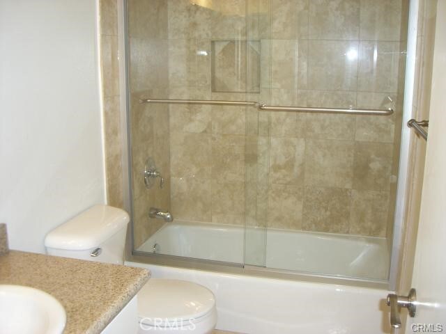 full bathroom featuring toilet, enclosed tub / shower combo, and vanity