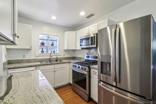 kitchen with dark hardwood / wood-style floors, white cabinetry, sink, stainless steel appliances, and light stone countertops