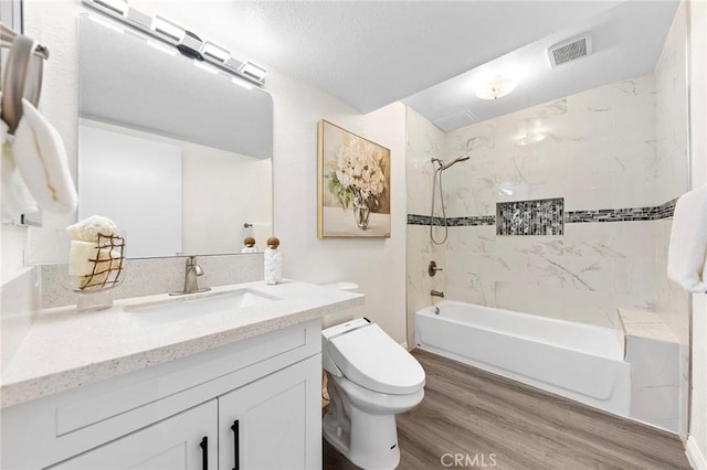 full bathroom with a textured ceiling, toilet, wood-type flooring, vanity, and tiled shower / bath combo