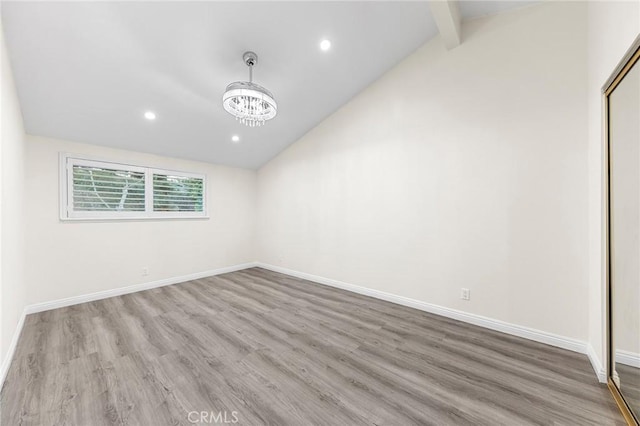 spare room featuring a notable chandelier, light wood-type flooring, and vaulted ceiling with beams