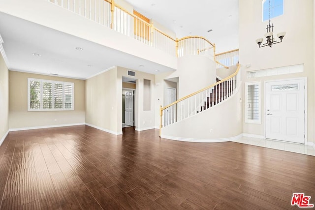 unfurnished living room featuring wood-type flooring, a high ceiling, crown molding, and a notable chandelier