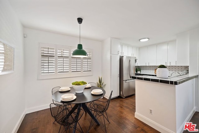 kitchen featuring white cabinetry, hanging light fixtures, stainless steel fridge, tile counters, and kitchen peninsula