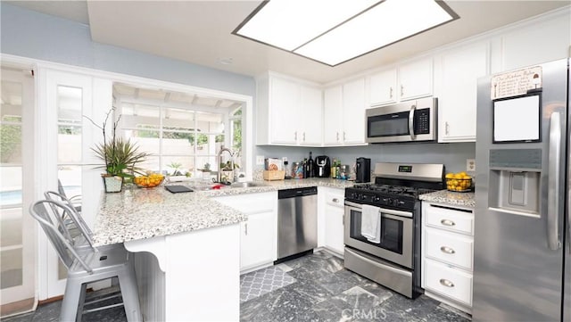 kitchen featuring appliances with stainless steel finishes, kitchen peninsula, a breakfast bar, light stone counters, and white cabinetry