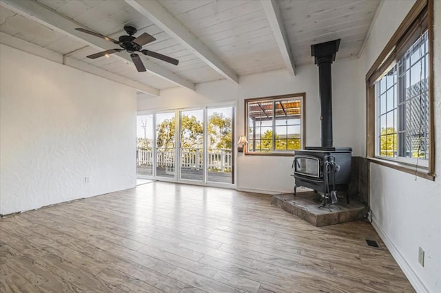 unfurnished sunroom with beam ceiling, a wealth of natural light, and a wood stove