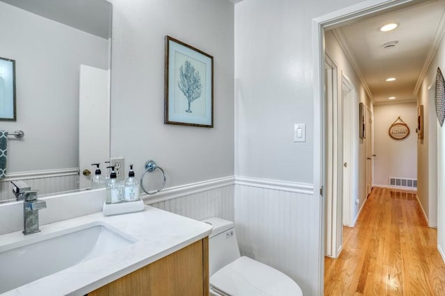 bathroom with toilet, ornamental molding, wood-type flooring, and vanity