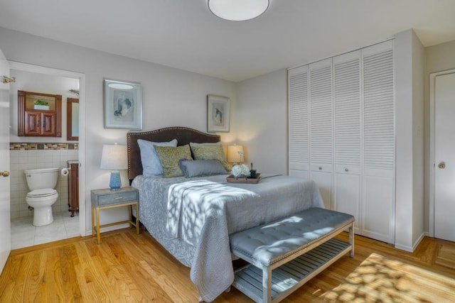 bedroom with tile walls, ensuite bathroom, light hardwood / wood-style flooring, and a closet