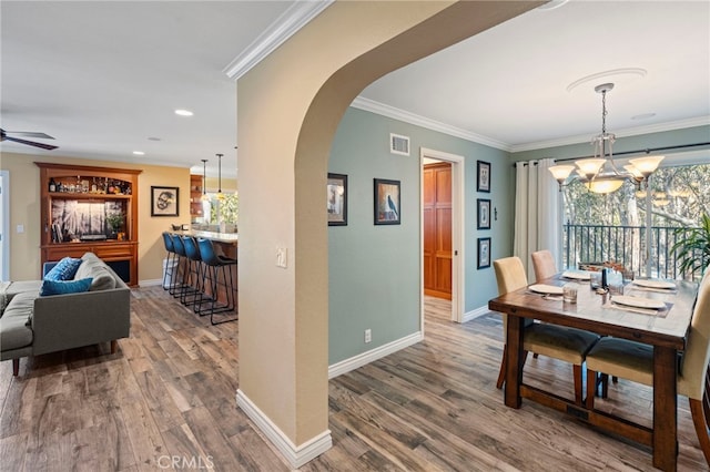 dining area with ceiling fan with notable chandelier, wood-type flooring, and ornamental molding