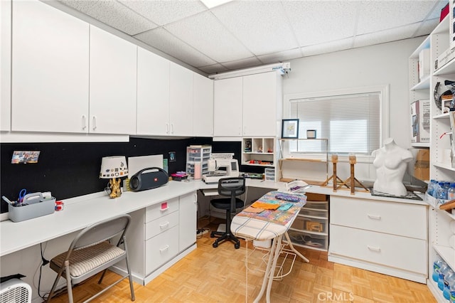 office featuring built in desk, a drop ceiling, and light parquet flooring