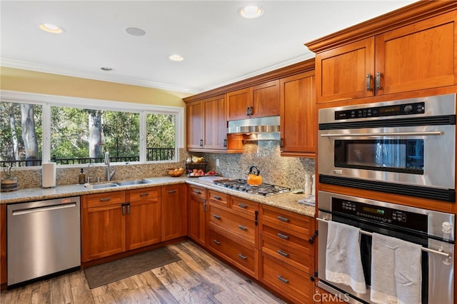 kitchen with light stone counters, hardwood / wood-style floors, crown molding, appliances with stainless steel finishes, and sink