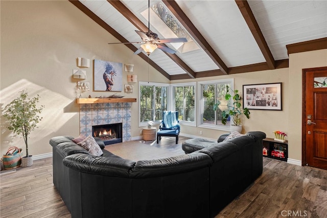 living room with ceiling fan, lofted ceiling with skylight, a tile fireplace, and wood-type flooring