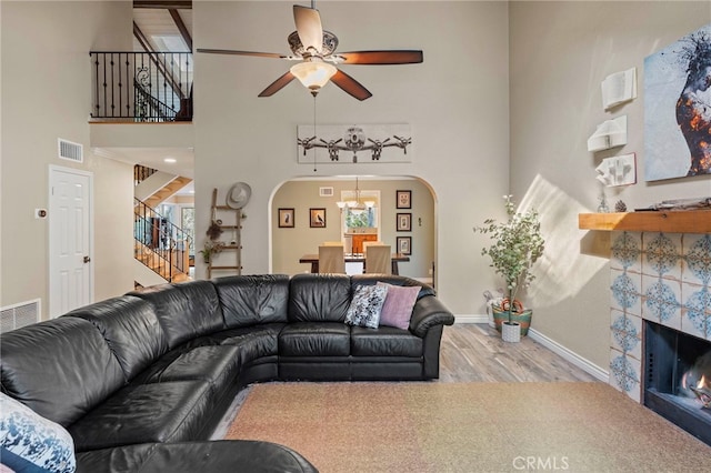 living room with a high ceiling, a tile fireplace, ceiling fan, and wood-type flooring