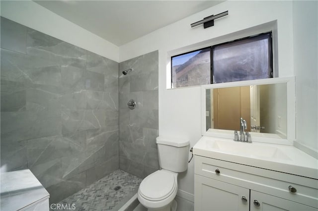 bathroom with toilet, tiled shower, and vanity