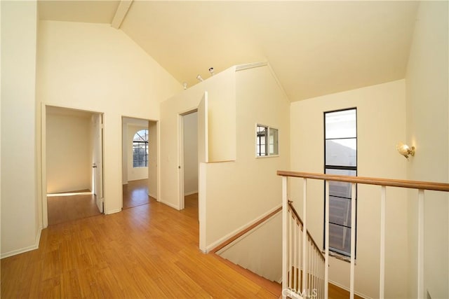 hallway featuring high vaulted ceiling, light hardwood / wood-style floors, and beam ceiling