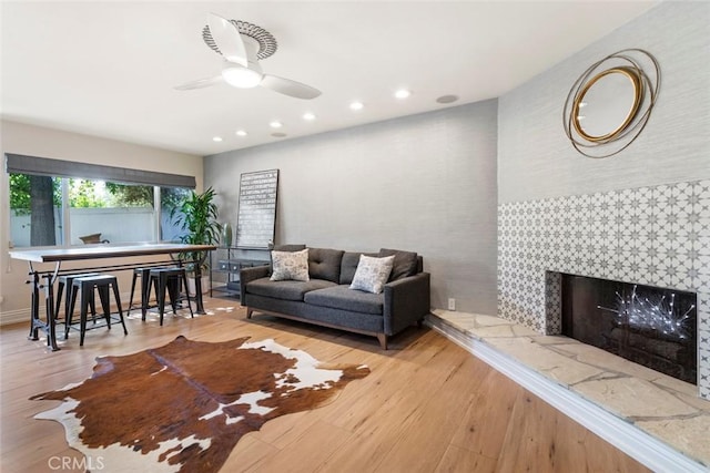 living room featuring ceiling fan, light wood-type flooring, a fireplace, and recessed lighting