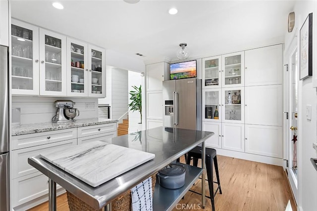 kitchen featuring light stone counters, high end fridge, glass insert cabinets, light wood-style floors, and white cabinetry