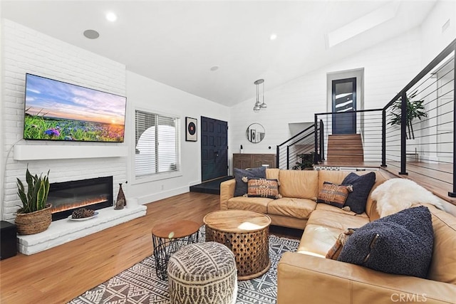 living area with a fireplace, wood finished floors, baseboards, vaulted ceiling, and stairway