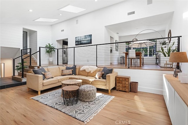 living area with a skylight, visible vents, stairs, light wood-style floors, and high vaulted ceiling