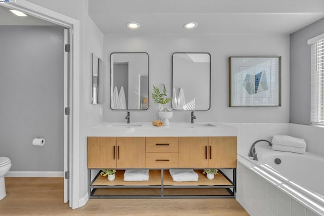 bathroom featuring toilet, vanity, hardwood / wood-style flooring, and tiled bath