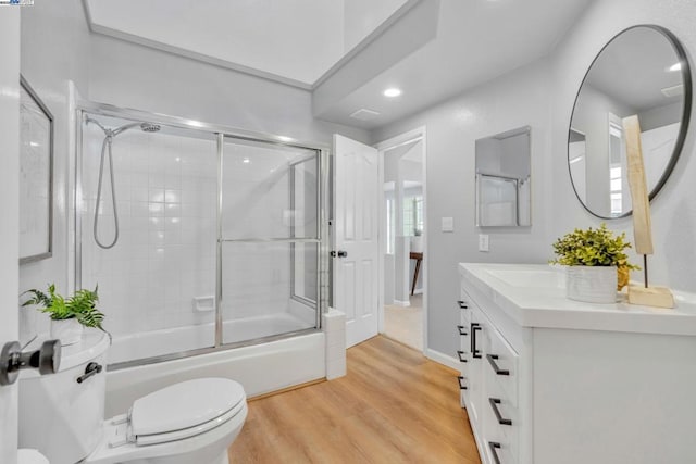 full bathroom with bath / shower combo with glass door, toilet, vanity, and wood-type flooring