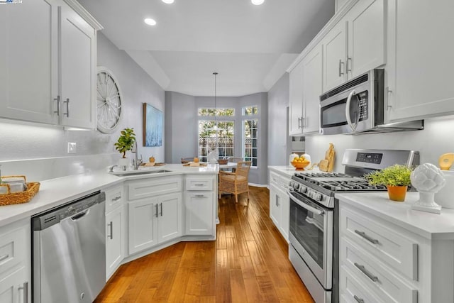 kitchen featuring pendant lighting, light hardwood / wood-style floors, white cabinets, appliances with stainless steel finishes, and sink