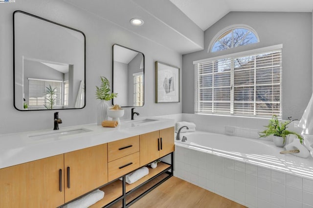 bathroom featuring tiled tub, vaulted ceiling, wood-type flooring, and vanity