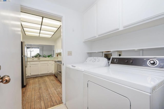 laundry room featuring washer and clothes dryer, cabinets, and light hardwood / wood-style flooring