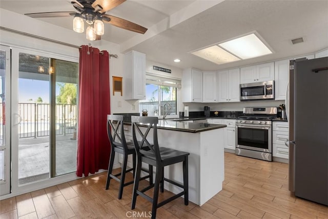 kitchen with stainless steel appliances, sink, white cabinets, a kitchen breakfast bar, and ceiling fan