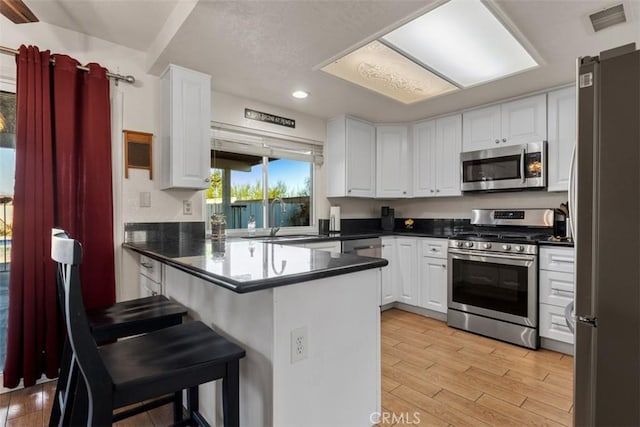 kitchen with sink, white cabinets, light hardwood / wood-style flooring, kitchen peninsula, and appliances with stainless steel finishes