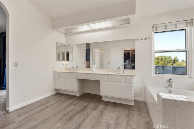 bathroom with tiled tub, vanity, and wood-type flooring