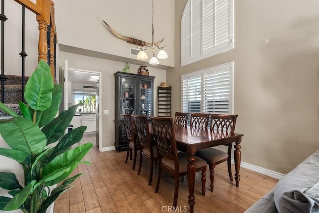 dining area featuring a high ceiling, light wood-type flooring, a chandelier, and a wealth of natural light