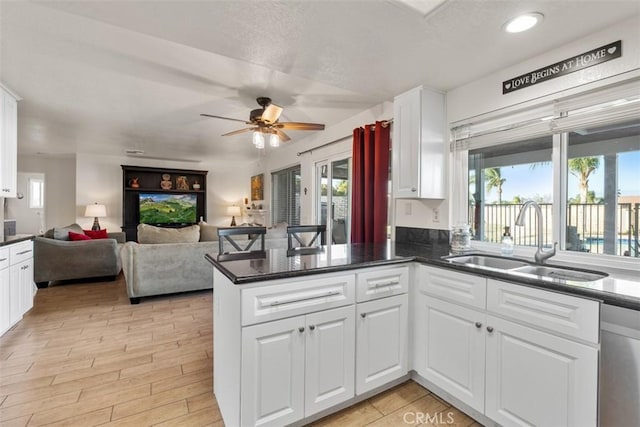 kitchen with dark stone countertops, kitchen peninsula, ceiling fan, sink, and white cabinetry