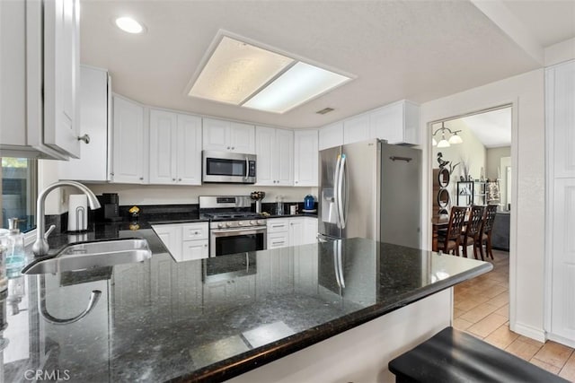 kitchen with dark stone countertops, appliances with stainless steel finishes, kitchen peninsula, white cabinets, and sink