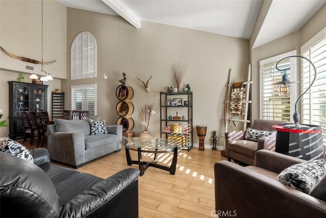 living room with a notable chandelier, light wood-type flooring, a wealth of natural light, and beamed ceiling