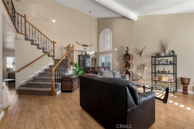 living room with beam ceiling, light wood-type flooring, an inviting chandelier, and plenty of natural light