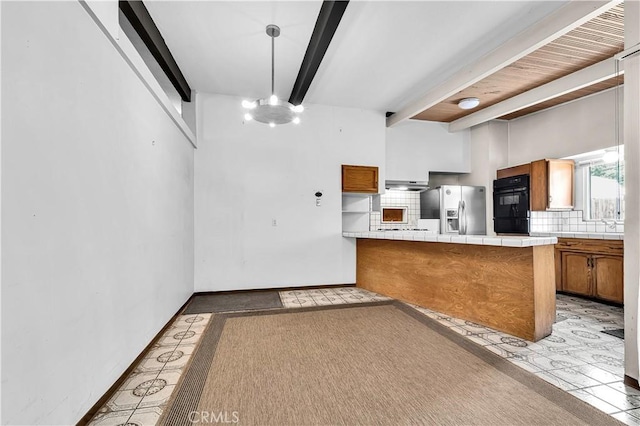 kitchen featuring tile counters, stainless steel refrigerator with ice dispenser, decorative backsplash, kitchen peninsula, and beam ceiling