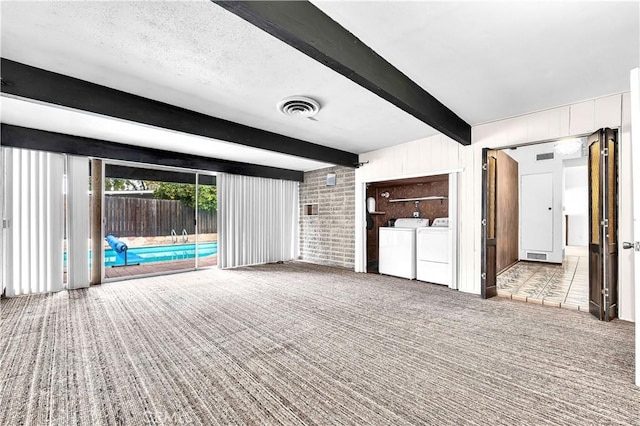 unfurnished living room with a textured ceiling, light colored carpet, beam ceiling, and washer / clothes dryer