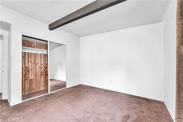 unfurnished bedroom featuring beam ceiling, a closet, wood walls, and dark colored carpet