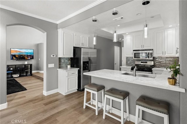 kitchen with a kitchen breakfast bar, appliances with stainless steel finishes, kitchen peninsula, white cabinetry, and backsplash